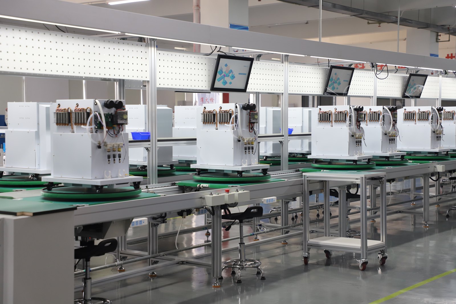 Rows of oxygen concentrator units on an assembly line, with tubing, valves and test displays visible on each unit